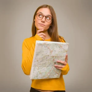 Eine junge Frau mit Brille und gelbem Pullover hält eine Landkarte in der Hand und blickt überlegend seitlich nach oben