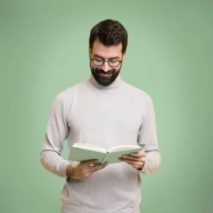 Dunkelhaariger Mann mit Bart und Brille schaut in ein Buch, er trägt einen hellgrauen Rollkragenpullover