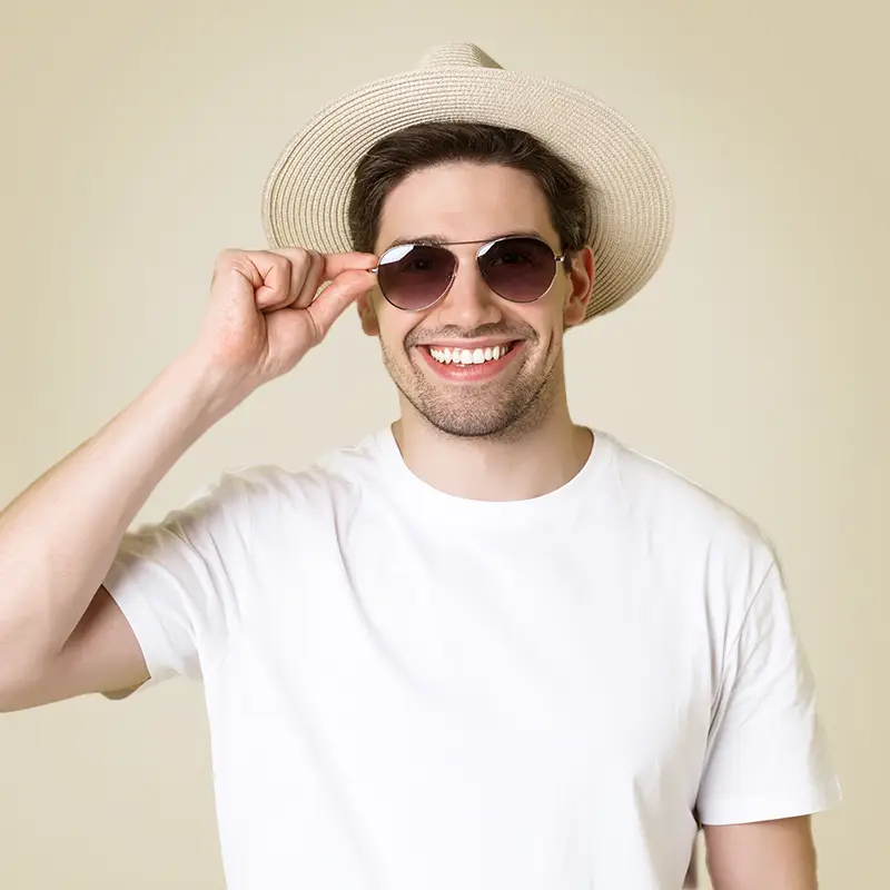 Ein grinsender junger Mann mit einem Strohhut und einer Sonnenbrille.